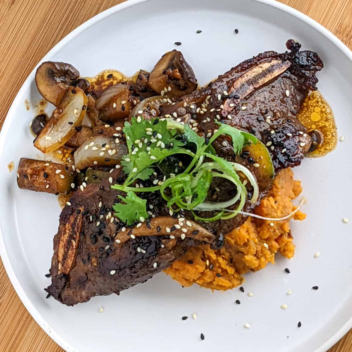 Korean short ribs over mashed sweet potatoes and sautéed vegetables on a white plate